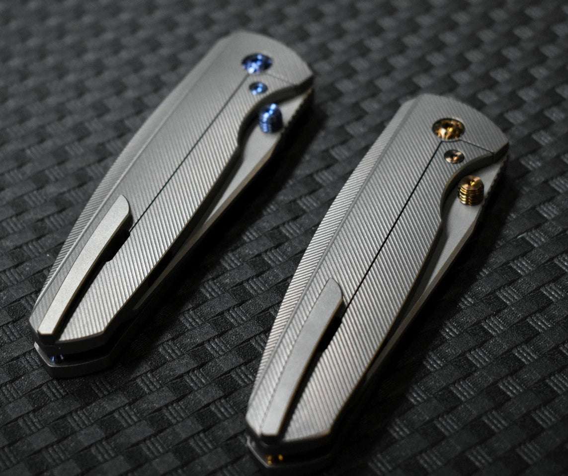 Two metallic pocket knives on a textured black surface
